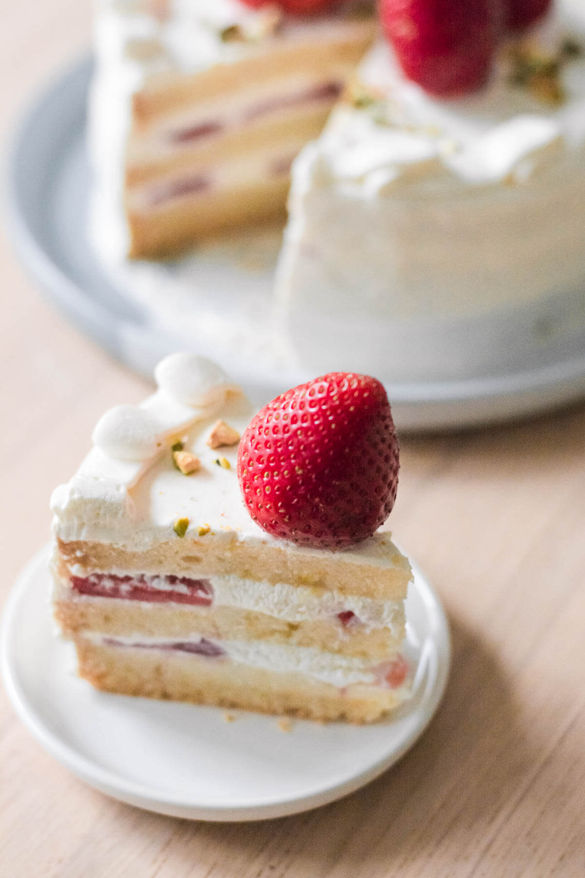 ein stück erdbeertorte mit ganzer torte im hintergrund