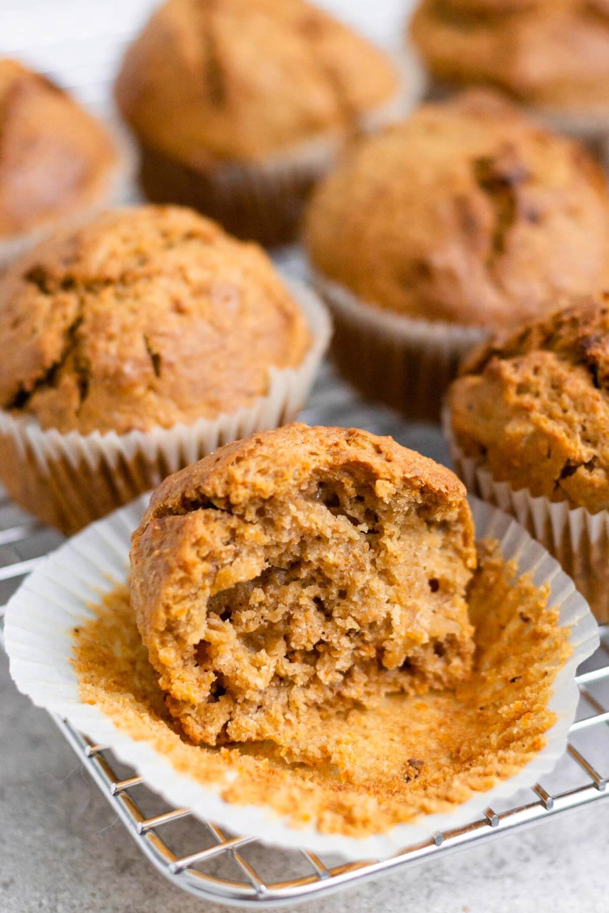 ein angebissener veganer karottenmuffin und ganze muffins im hintergrund.