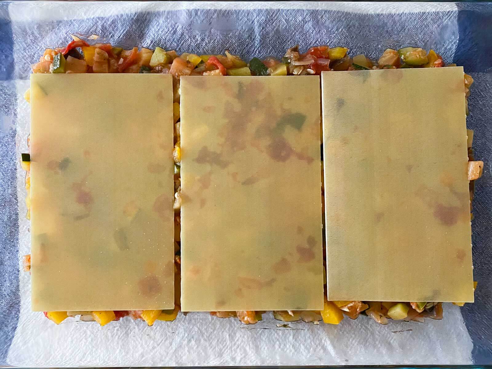 drei lasagneplatten auf ratatouillegemüse in einer auflaufform.